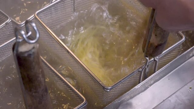 沸騰したお湯の中でパスタを茹でる動作。テボ（振りザル）の中で麺が躍り、湯気が上がる様子を捉えた映像。飲食店メニュー、イタリアン料理の紹介、調理工程をテーマにした広告や映像素材に。 | Boiling pasta noodles in a deep strainer.