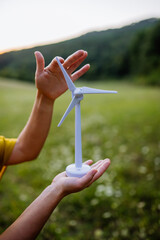 Close up of hands holding model of wind turibe in nature. Concept of ecology future and renewable...