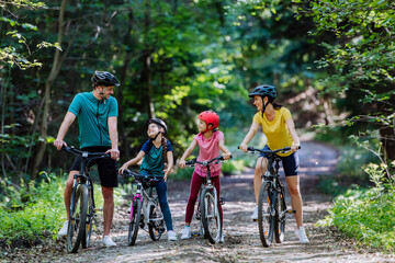 Young family with little children preapring for bike ride, standing with bicycles in nature.