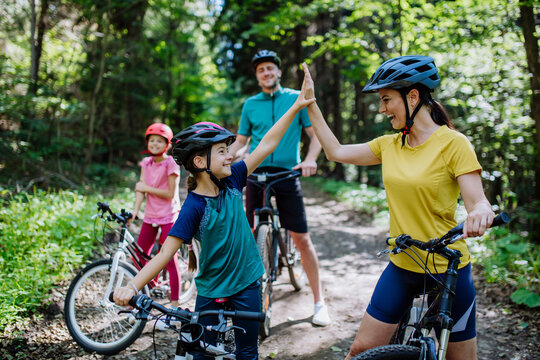 Young family with little children preapring for bike ride, standing with bicycles in nature and high fiving.