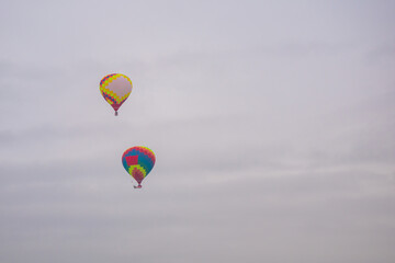 Two colorful hot air balloons flying against grey sky at Winter aerostat festival. Freedom, sport, aircraft concept