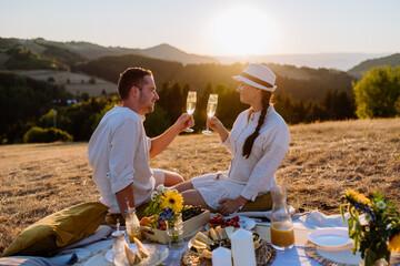Attractive couple in love enjoying picnic and drinking wine on the hill at sunset.