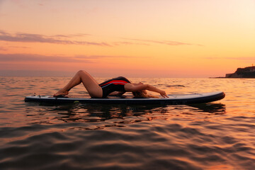 Sexy young woman posing lying at sup board in the ocean. Copy space. Sunset at the background. The...