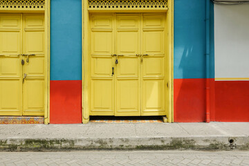 colorful facade of a traditional house in a colombian village. Two large closed yellow gates in a blue and red wall. An empty scene with sidewalk. Looks caribian and mediterranean. 