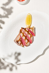 Grilled tuna steak on light background with shadows. Grilled tuna with lemon on white table....