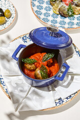Traditional italian meatballs in tomato sauce on white table. Beef meatballs in ceramic pot in italian style with tomato and basil. Main course from meat in elegant style. Homemade meatballs.
