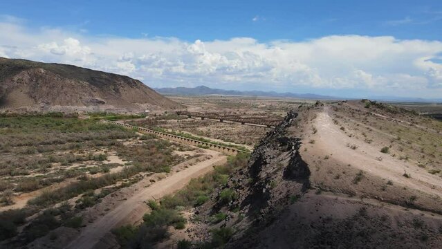 Drone Panning around a cliff revealing an old rustic steel bridge on a sunny day , blue sky with large white clouds Gillespie Dam and Bridge, Gila river