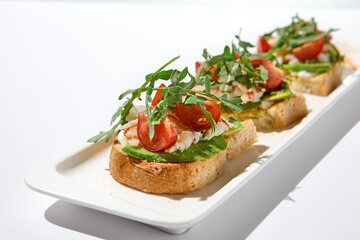 Aesthetic composition with shrimp bruschetta on white background over white wall. Italian bruschetta with shrimp, tomatoes and arugula on fine dining in summer. Elegant menu concept.