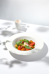 Salad with octopus, baked potatoes and poached egg on white table with hard shadows. Seafood salad with vegetables and potatoes in summer menu restaurant. Octopus and eggs salad in modern style.