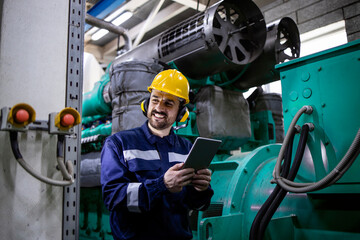 Portrait of power plant worker with digital tablet standing by gas generator producing electricity.
