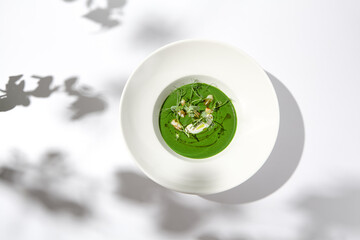 Healthy green cream soup with fish and pea. Spinach soup puree on white plate with shadows. Summer...