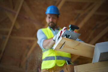 Low angle view of handyman working with circular saw on wooden construction site, diy eco-friendly...