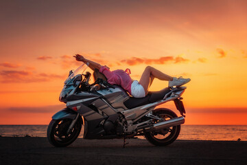 Fototapeta na wymiar Freedom. Sexy young woman posing on the motorcycle. Golden sunset and motorbike on the background. Side view. Concept of World Motorcyclist Day and moto trips