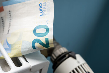 Euro banknotes in a radiator and a thermostat knob at a minimum, close-up. Concept of energy crisis...