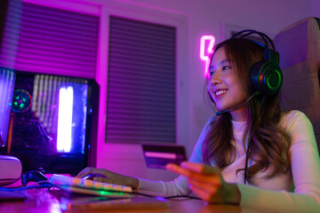 Top up online game with credit card concept. Gamer and E-Sport online of Asian woman playing online computer video game with lighting effect, broadcast streaming live at home. Gamer and E-Sport gaming © Kiattisak