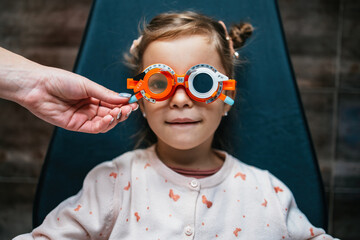 Beautiful and adorable little girl with optometry glasses receiving ophthalmology treatment. Doctor...