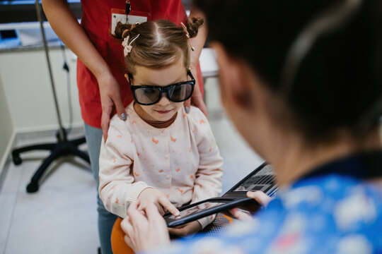 Beautiful and adorable little girl receiving ophthalmology treatment. Doctor ophthalmologist using pinhole glasses for eyesight improvements exercises.