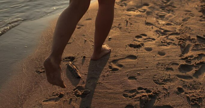 Close-up of the legs and feet of a young woman walking along the shore of the beach at sunset. Relaxation, rest, enjoyment.