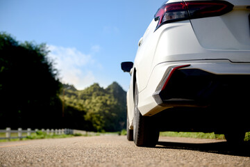Close-up rear view of a white car with mountains and sky on the road.