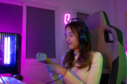 Wrist Pain Concept. Gamer And E-Sport Online Of Asian Woman Playing Online Computer Video Game With Lighting Effect, Broadcast Streaming Live At Home. Her Use Her Wrist For A Long Time.