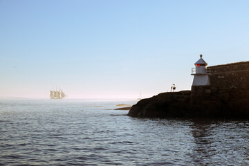 Lighthouse on the coast behind an old sailing ship on the horizon