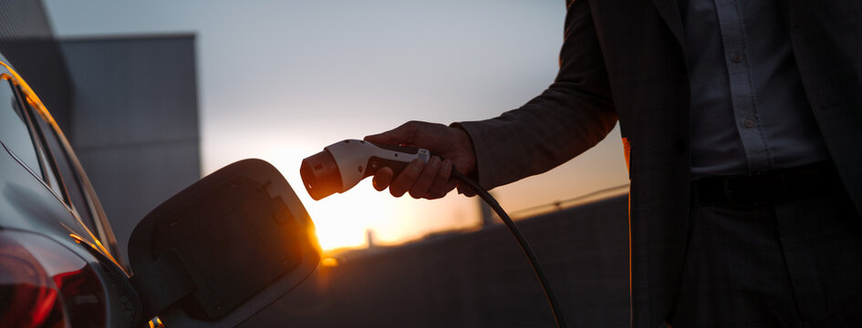 Man holding power supply cable at electric vehicle charging station, closeup