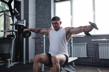 Fototapeta na wymiar Big muscular male bodybuilder working out with dumbbells, doing lateral raise exercise at gym