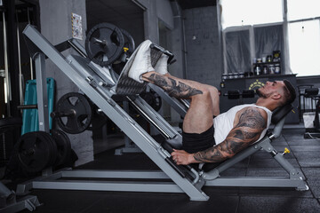 Full length profile shot of a big muscular bodybuilder doing leg press exercise at gym