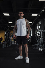 Fototapeta na wymiar Vertical full length shot of a big muscular tattooed sportsman standing in the gym