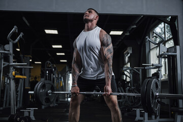 Fototapeta na wymiar Huge muscular tattooed bodybuilder lifting heavy barbell at gym