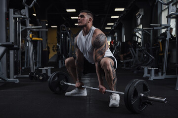 Fototapeta na wymiar Full length shot of a huge muscular tattooed fitness man working out with barbell at gym