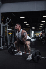 Fototapeta na wymiar Vertical full length shot of a strong muscular tattooed male athlete working out at fumctional training gym, lifting barbell