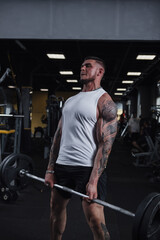 Fototapeta na wymiar Vertical shot of a ripped tattooed sportsman lifting heavy barbell