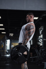 Fototapeta na wymiar Vertical profile shot of a big muscular bodybuilder lifting heavy barbell