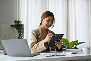 Youngcheerful smiling Asian accountant writing notary in clipboard on white desk with office suppliers.