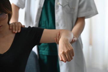 Focused on professional masseur medic stretches woman's arm muscles to recover from elbow injury.