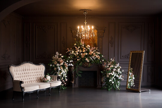 Black room interior with a vintage sofa, chandelier, mirror and fireplace decorated with flowers