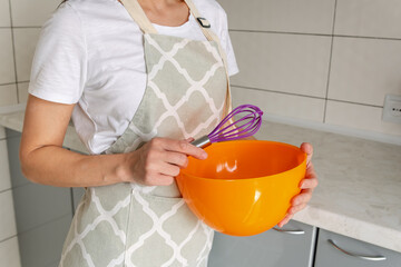 Female cooking at kitchen table, preparing dough for baking in bowl. Woman cooks home food from flour and eggs. Homemade bakery preparation. Happy chef whisking cream. Smiling woman using whisk