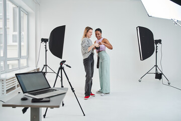 Cheerful female model smiling toothy while looking at the result of the photo session
