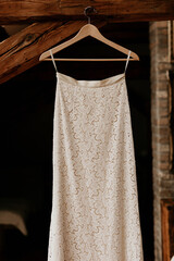 A beautiful lace wedding dress is hanging on a wooden hanger in the attic. Stunning white details, pretty style. Black background copy space. Big day preparation design.