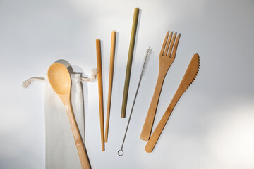 Eco wooden cutlery, spoon, fork, knife and bamboo straws on a textile bag on a white background. Top view
