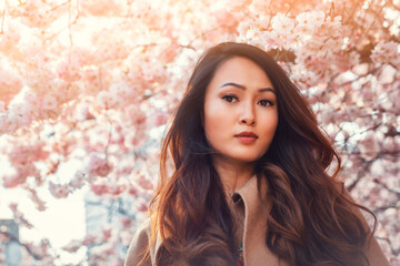 Young Asian woman, in front of blossoming cherry tree in the spring time 