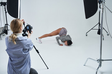 Caucasian photographer shooting her multiracial model while holding camera and standing at the...