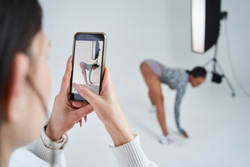 Female assistant shooting backstage at the smartphone while multiracial dancer posing at the studio