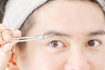 眉バサミで眉毛を切る男性のクローズアップ