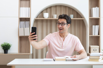 Young smiling handsome man holding smartphone while studying at home