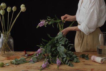 girl florist collects a bouquet in a flower workshop on a dark background. layout for floristry