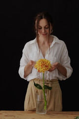 girl holding a dahlia flower in a glass vase on a wooden table, dark background, mockup