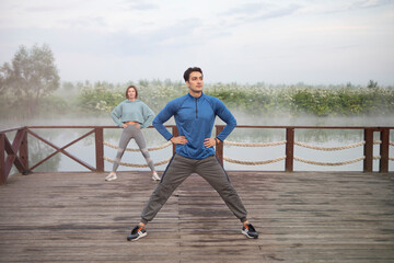 Young sporty couple training on wooden platform on the foggy river 