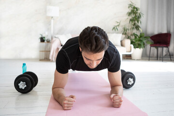 Fototapeta na wymiar Handsome sporty man doing plank exercise online at living room. Healthy lifestyle and home training concept